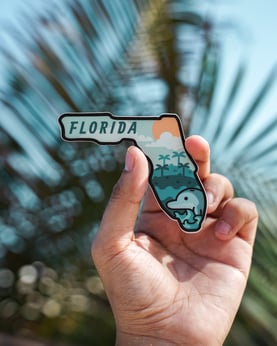 Someone holds up a Florida-shaped fridge magnet