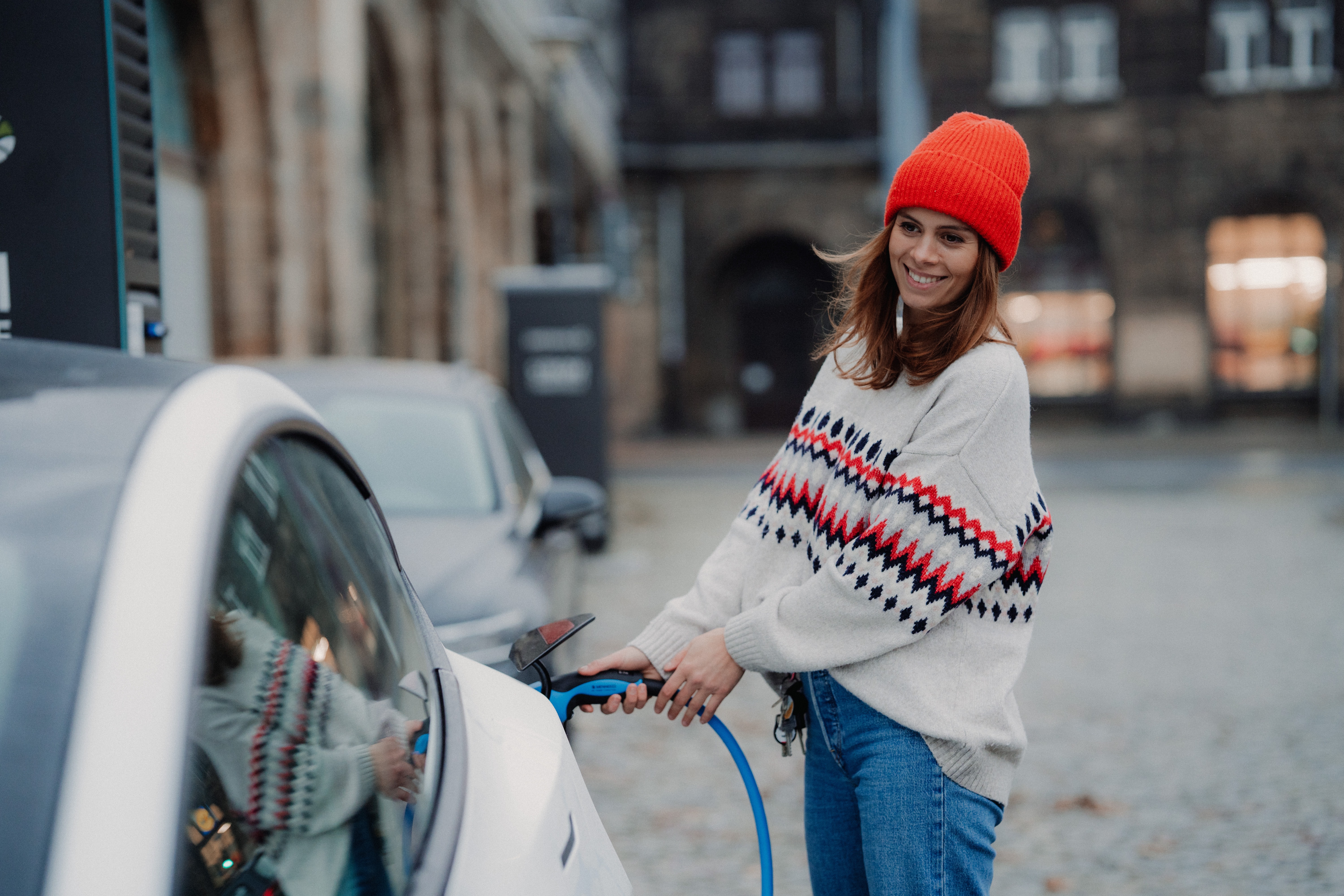 A young woman in a red hat charges her electric vehicle