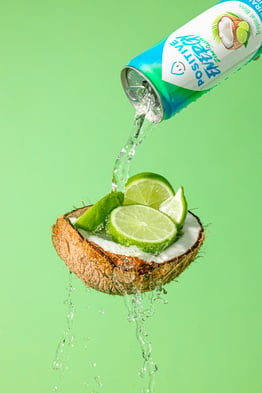 A can of healthy-looking energy drink — "Positive Energy" — being poured onto an open coconut with lime segments