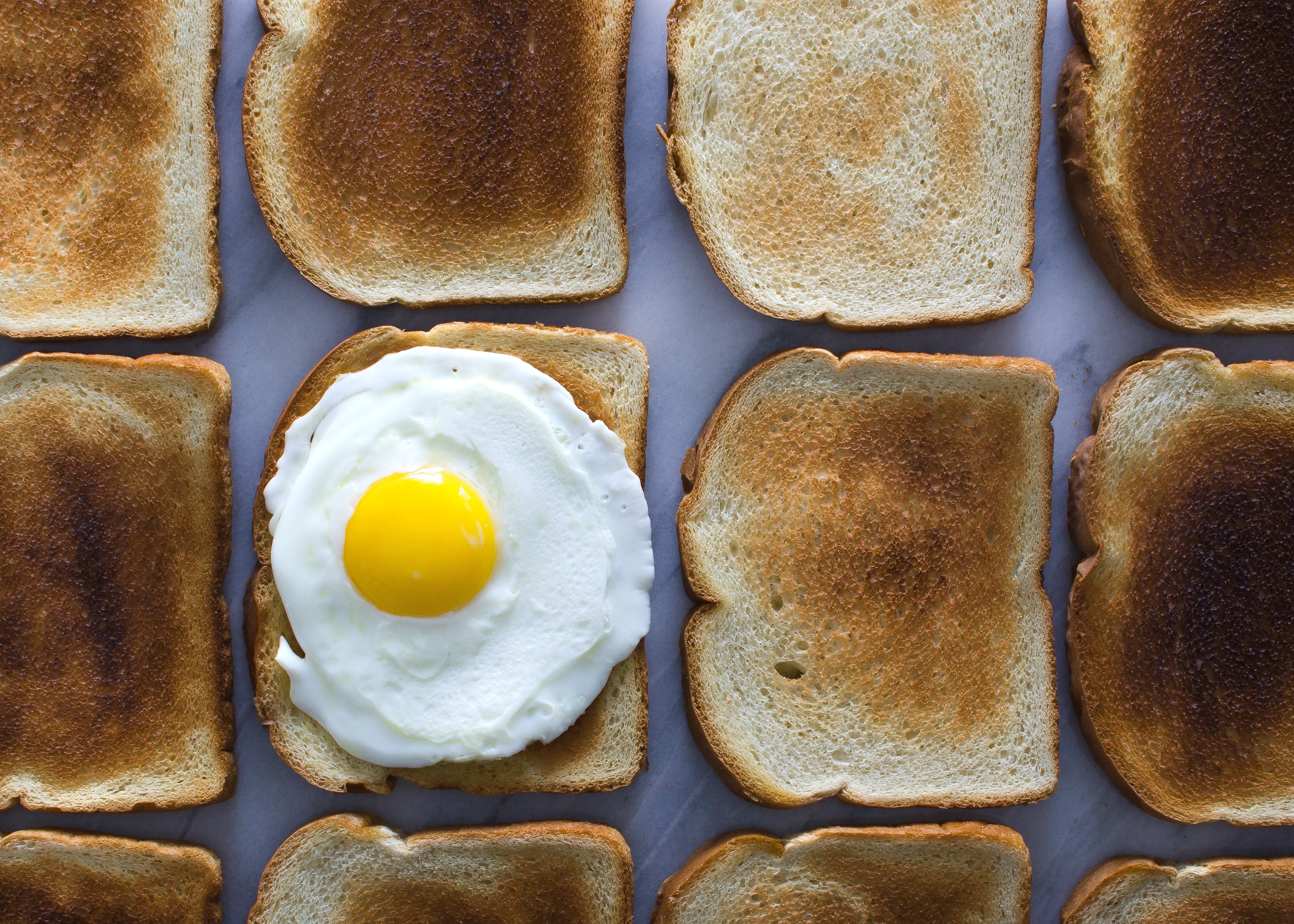 Several slices of toast from a bread brand, placed on a work surface, one with a fried egg