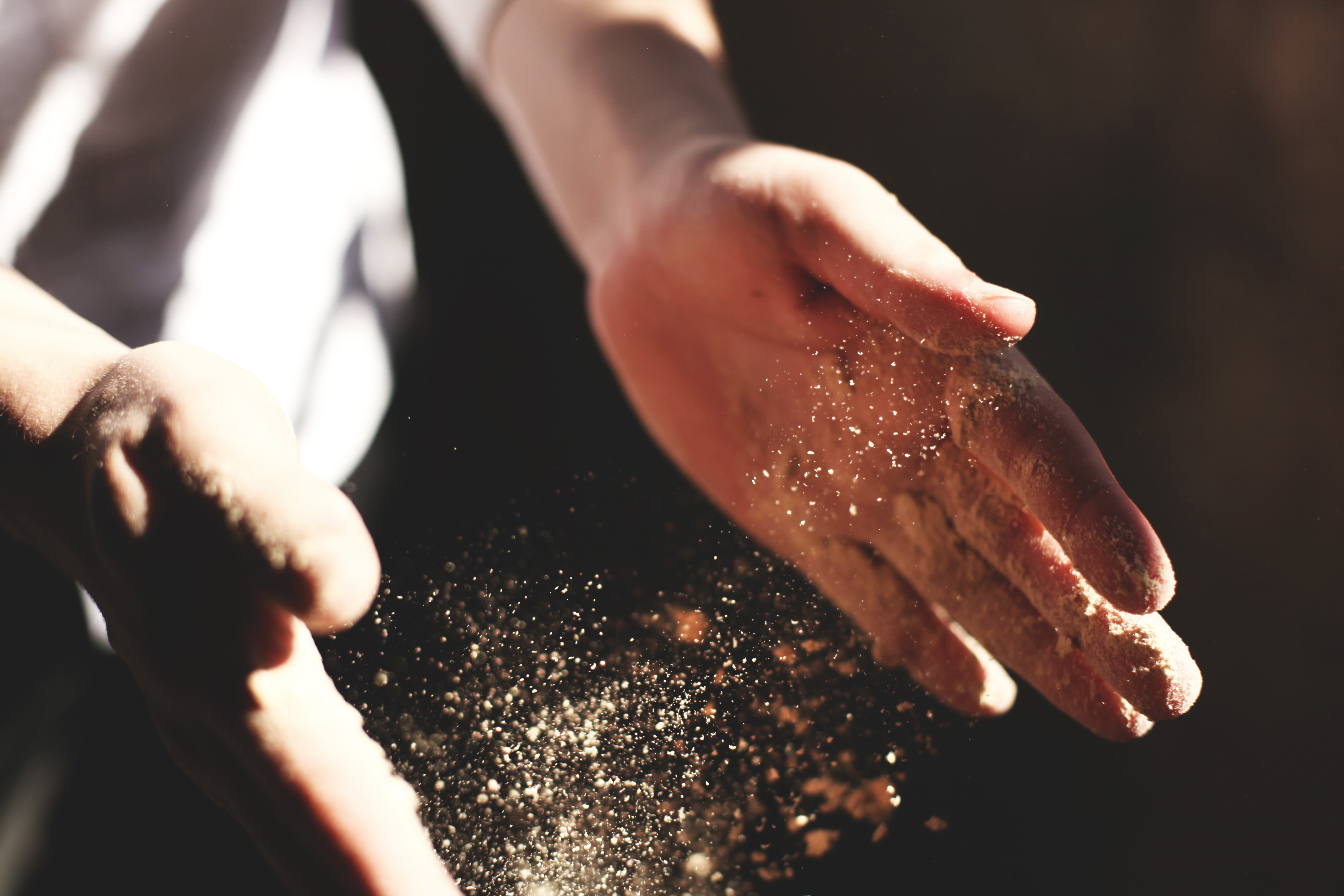 A close-up photo of a baker clapping flour between his hands