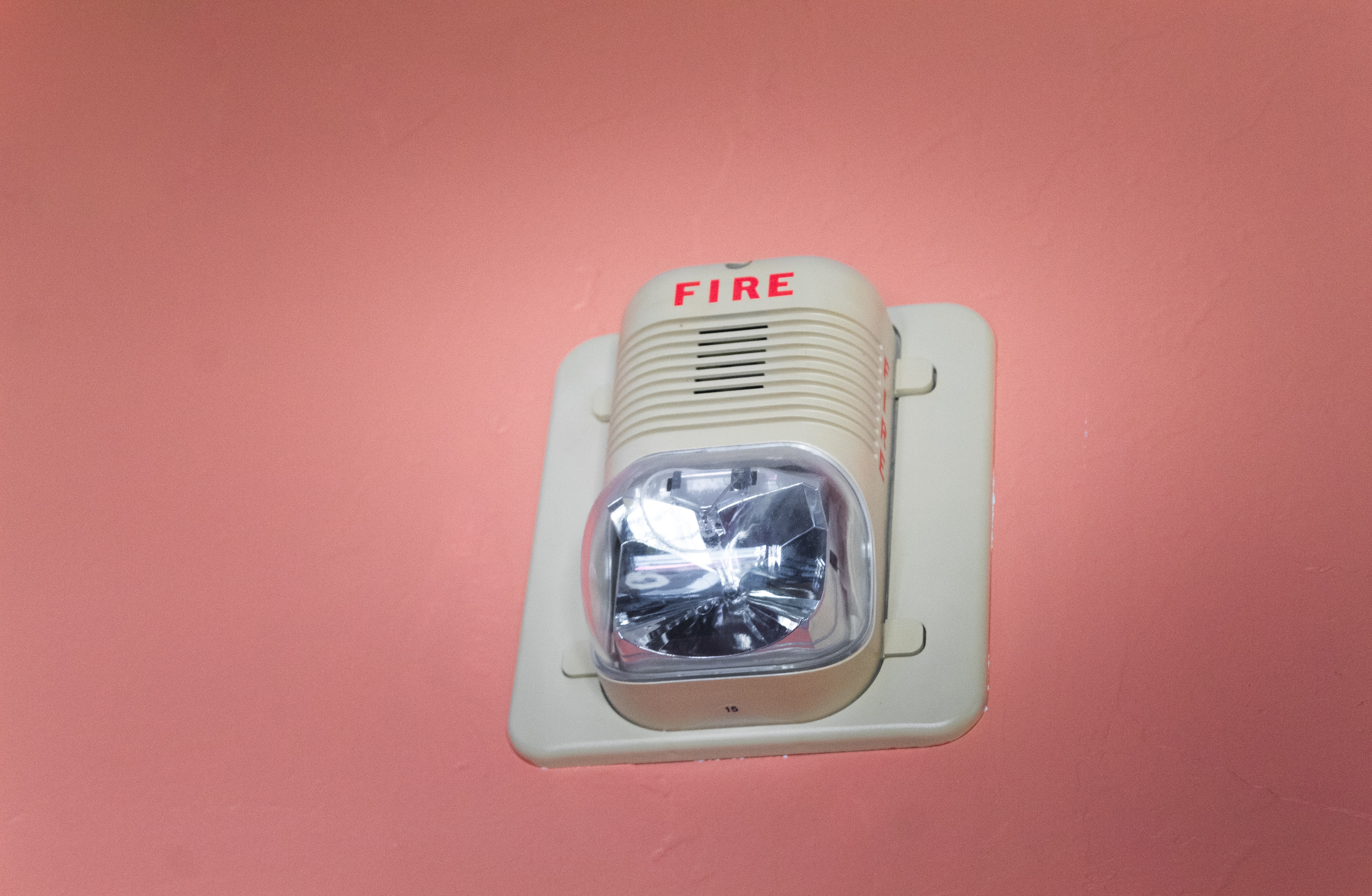 A picture of a fire alarm mounted onto a pink wall