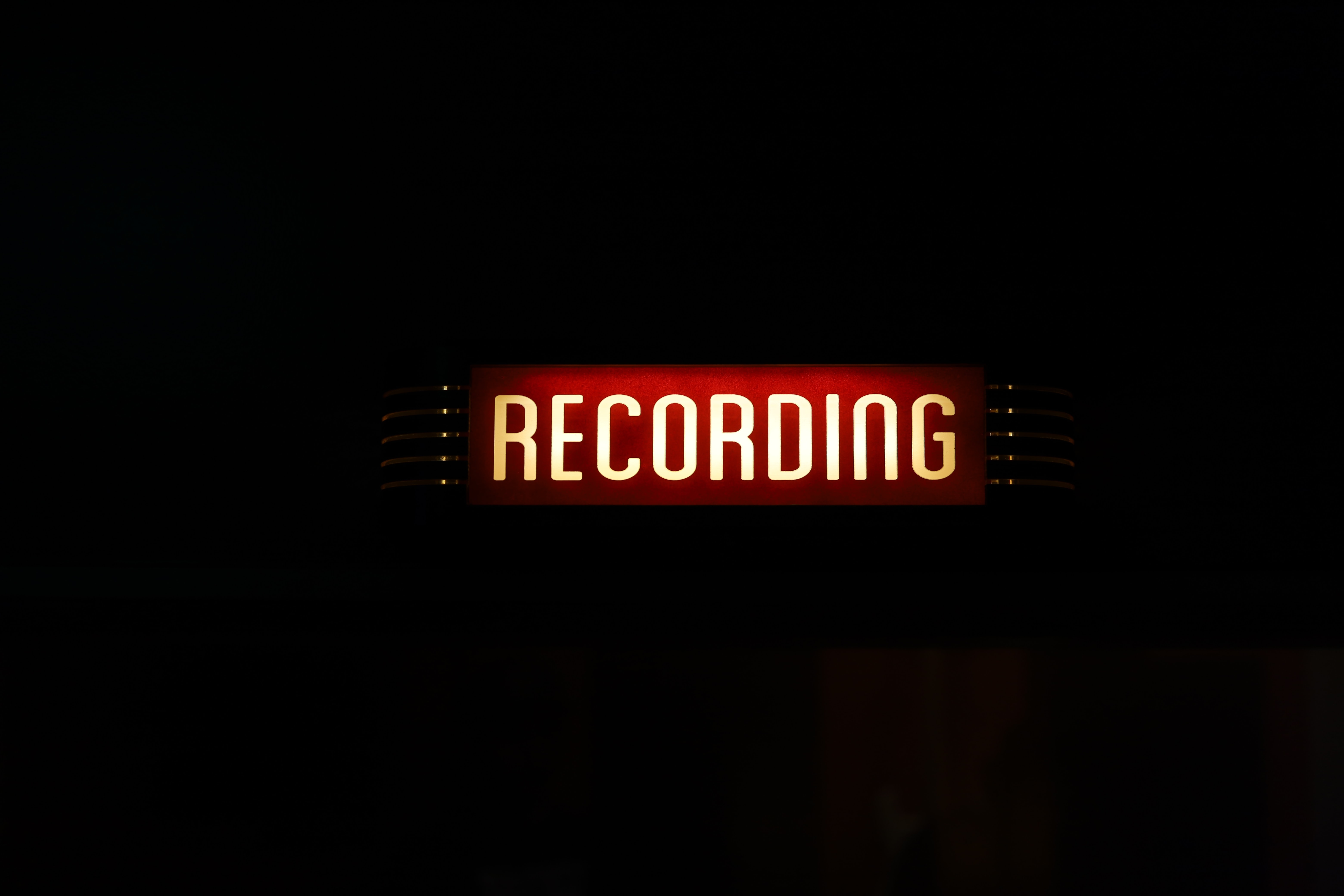 A red neon sign reading 'Recording' — brand voice isn't necessarily spoken out loud, but it can be used in scripts and voice overs