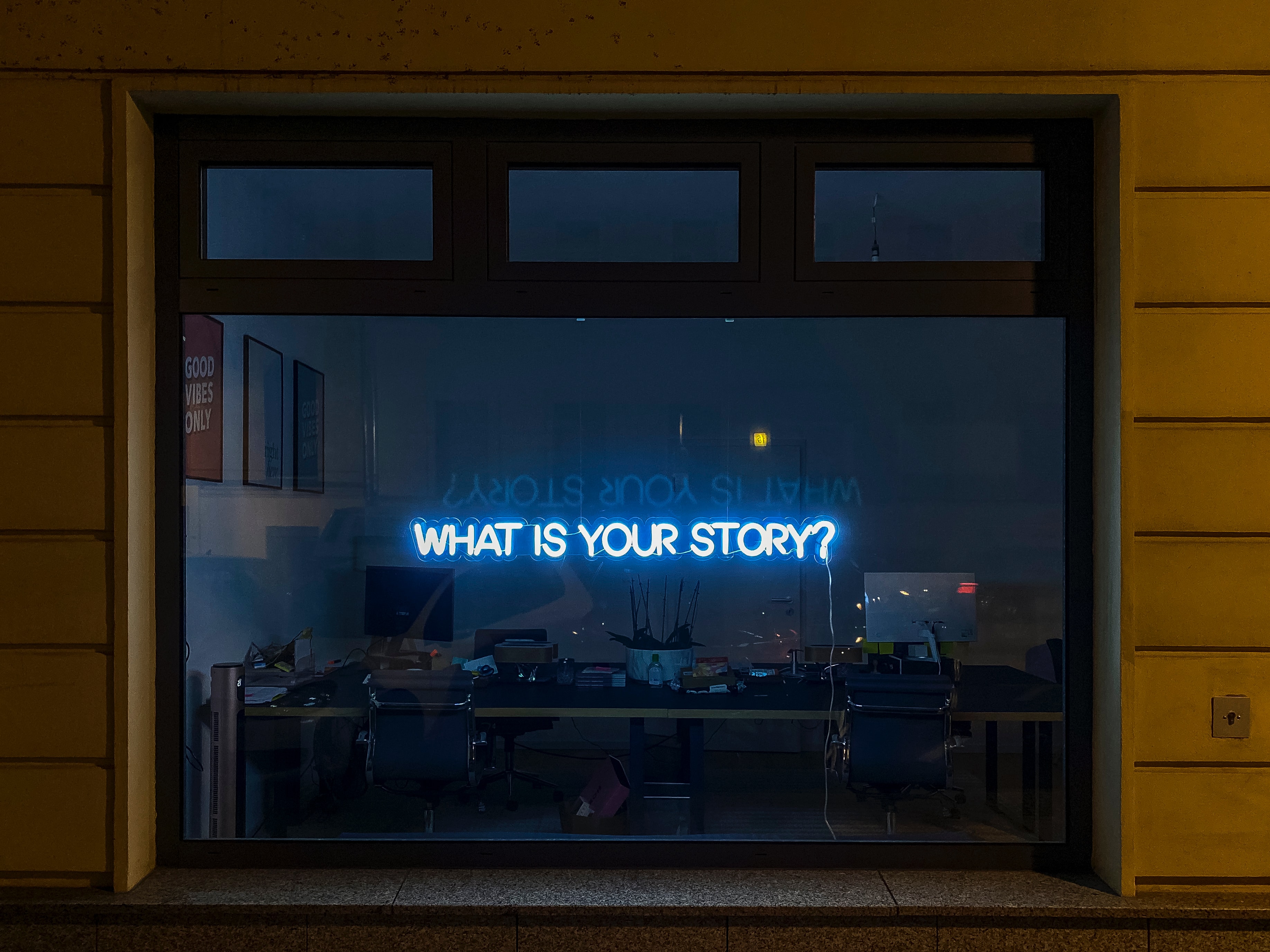 A blue neon sign in a window display reads 'What is your story?'