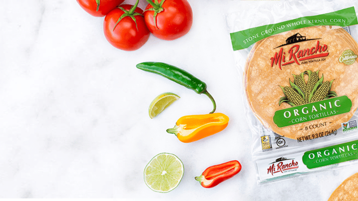 Mi Rancho organic corn tortilla packaging staged on a white marble countertop with sliced peppers, lime, and fresh tomato