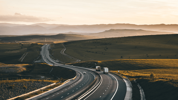 Trucks driving down a highway amongst hilly landscape at dusk or dawn