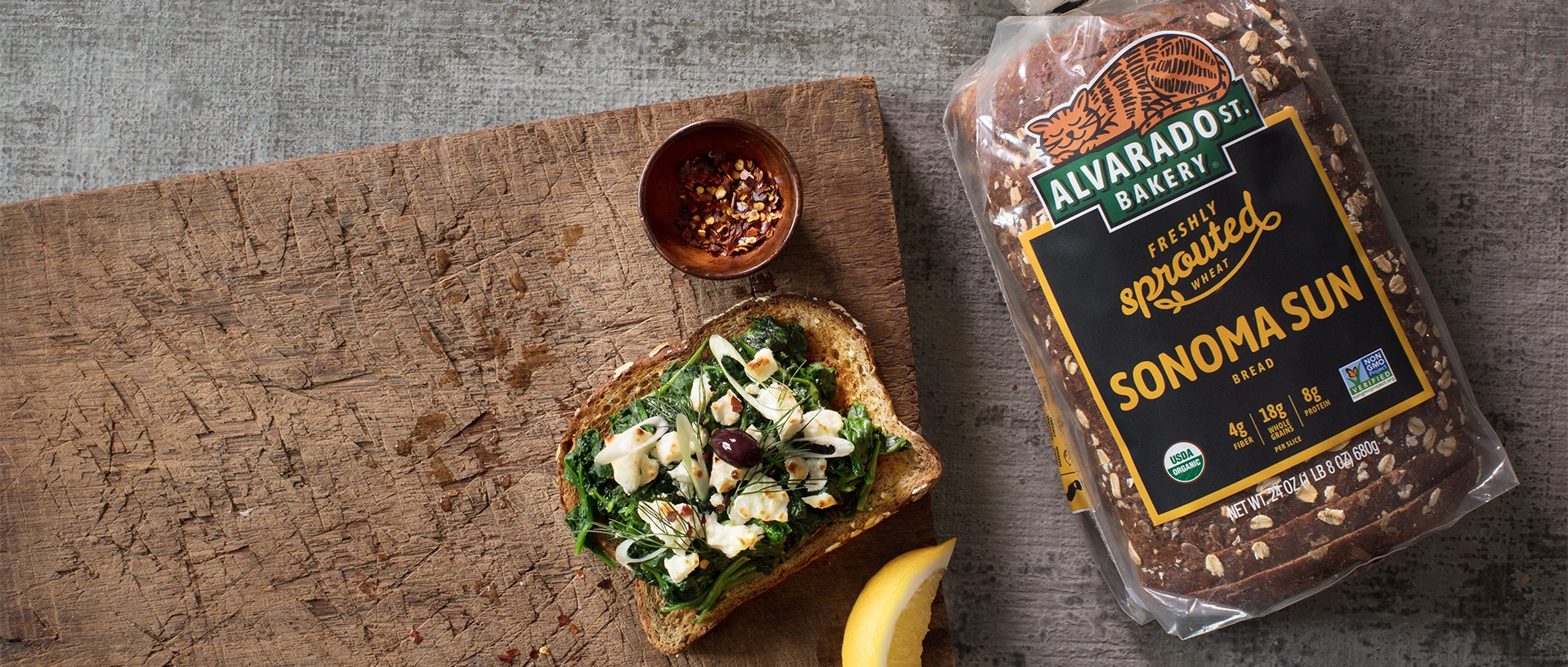 Package of Sonoma Sun Alvarado Street Bakery bread next to a cutting board with an open-faced sandwich on top