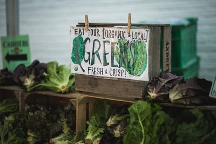Sign reading "eat your local greens" above a display of produce.