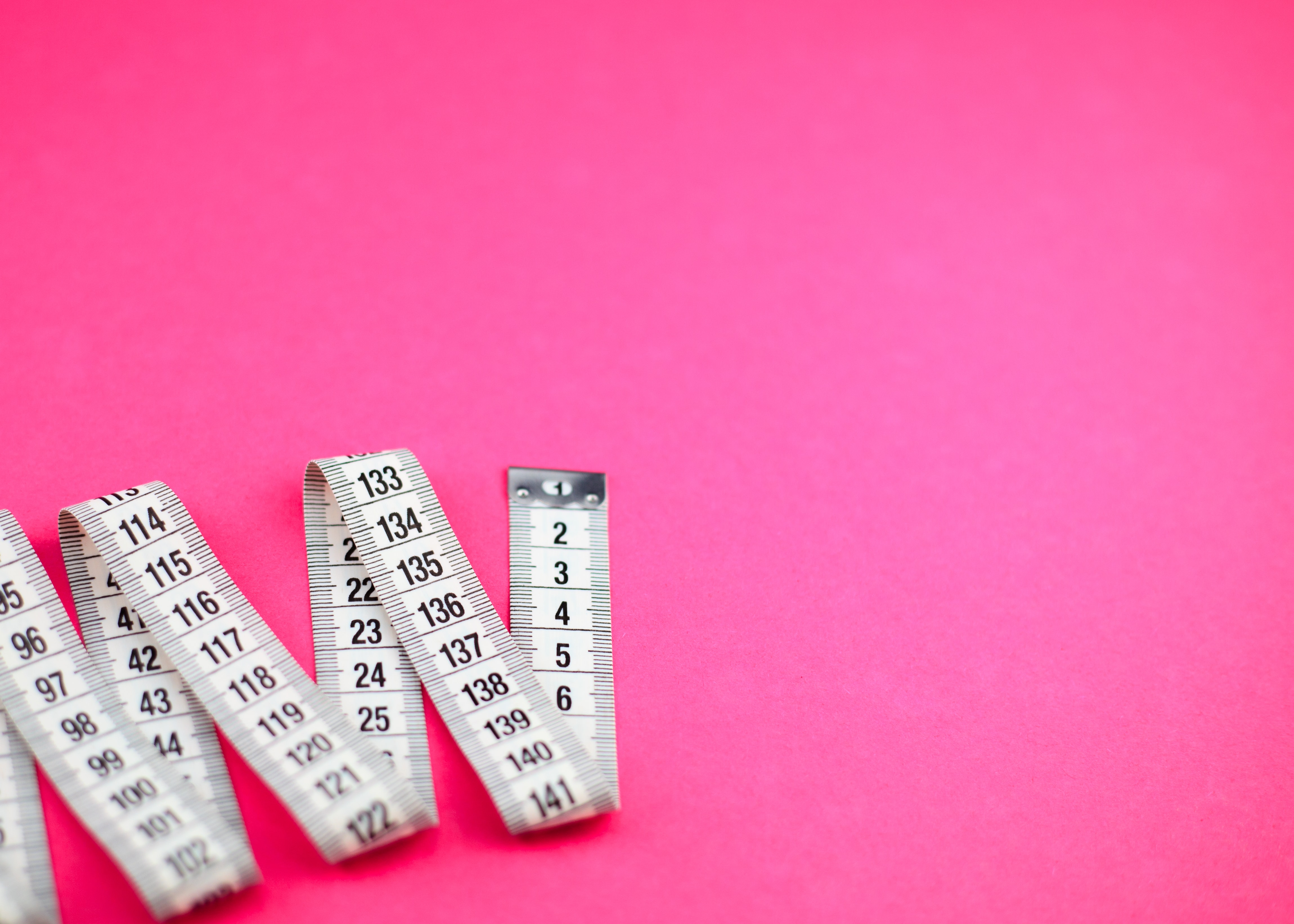 A white measuring tape against a hot pink background