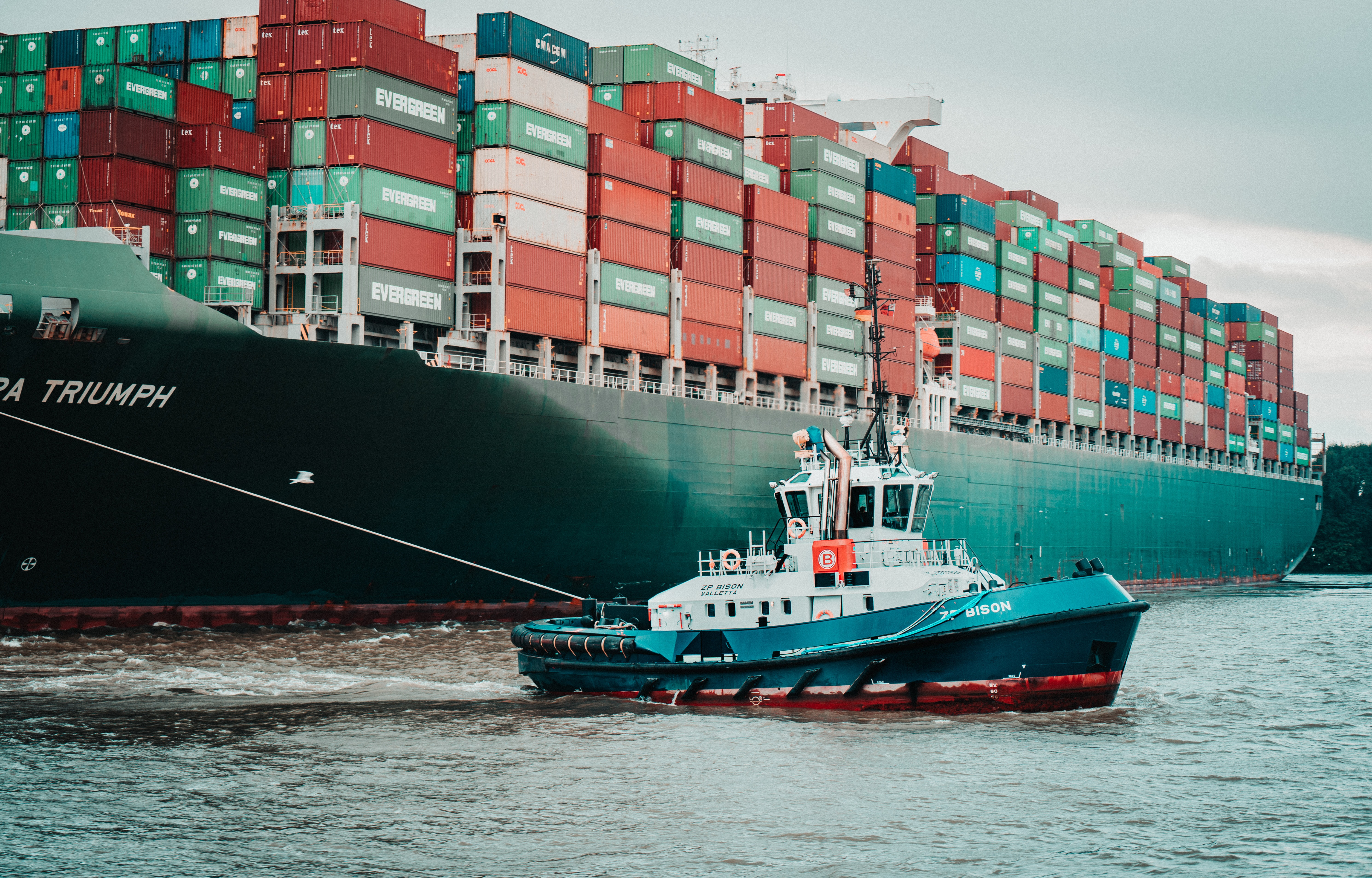 A tug boat pulling a huge container ship for distribution supply chains