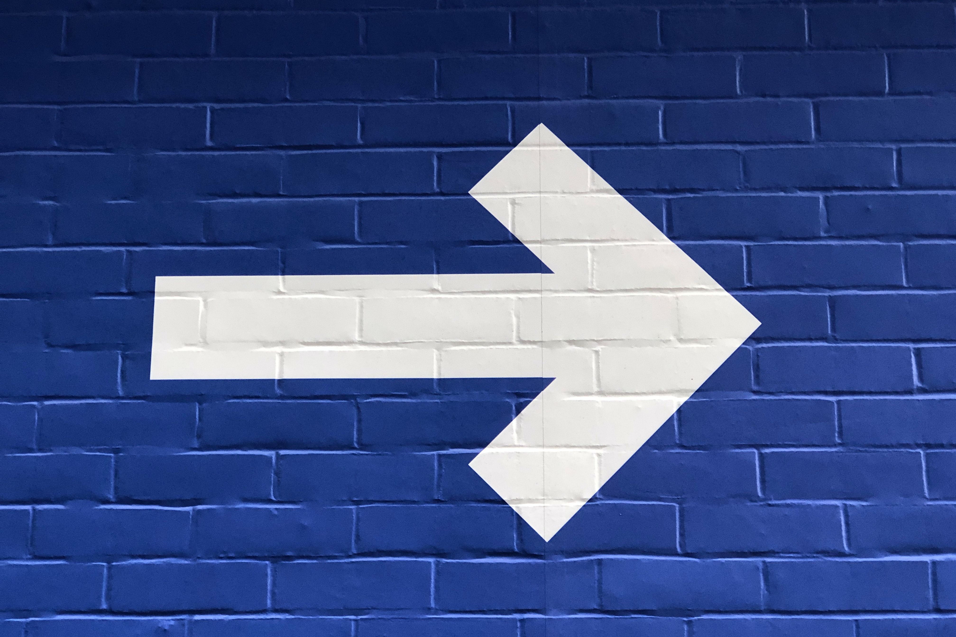 A white arrow painted on a blue brick wall