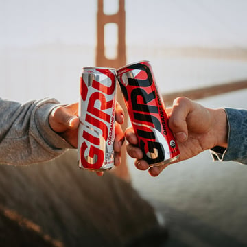 Guru Energy Drink cans cheers-ing. Golden Gate Bridge in the background