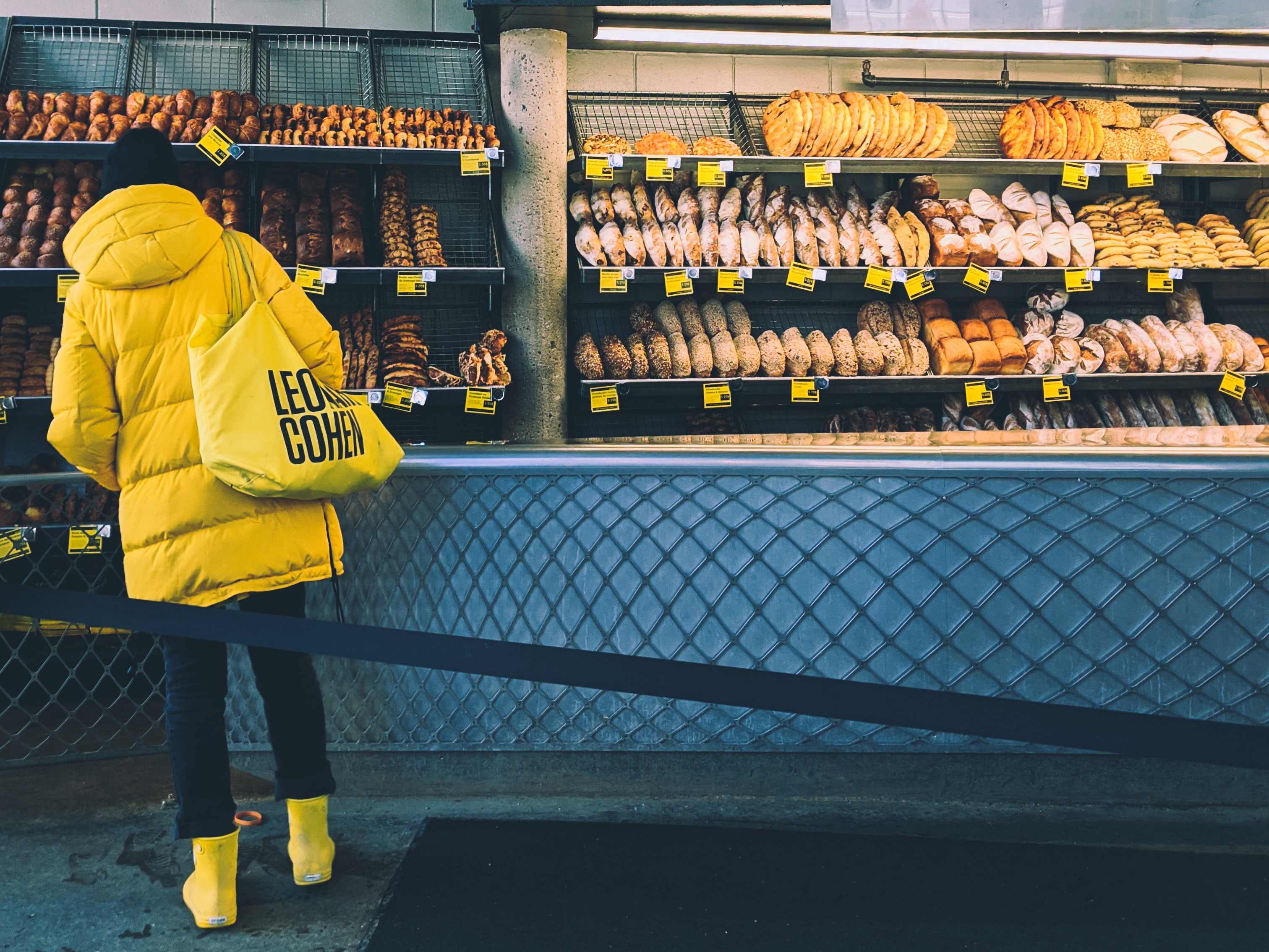 A woman in a yellow coat with a yellow bag browses a fully-stocked bakery aisle