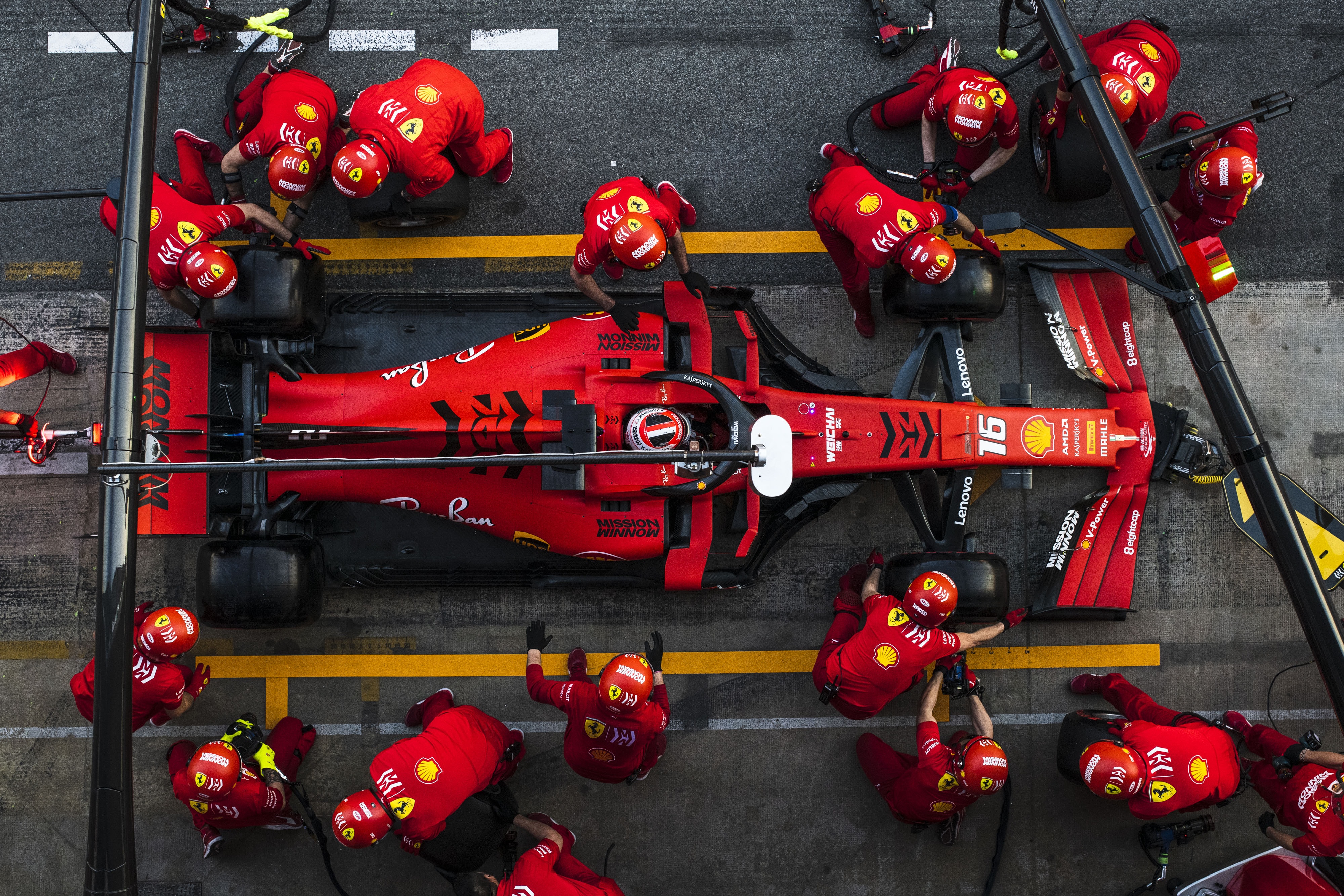 A red Formula 1-style racecar being worked on by pit crew, all in red uniforms