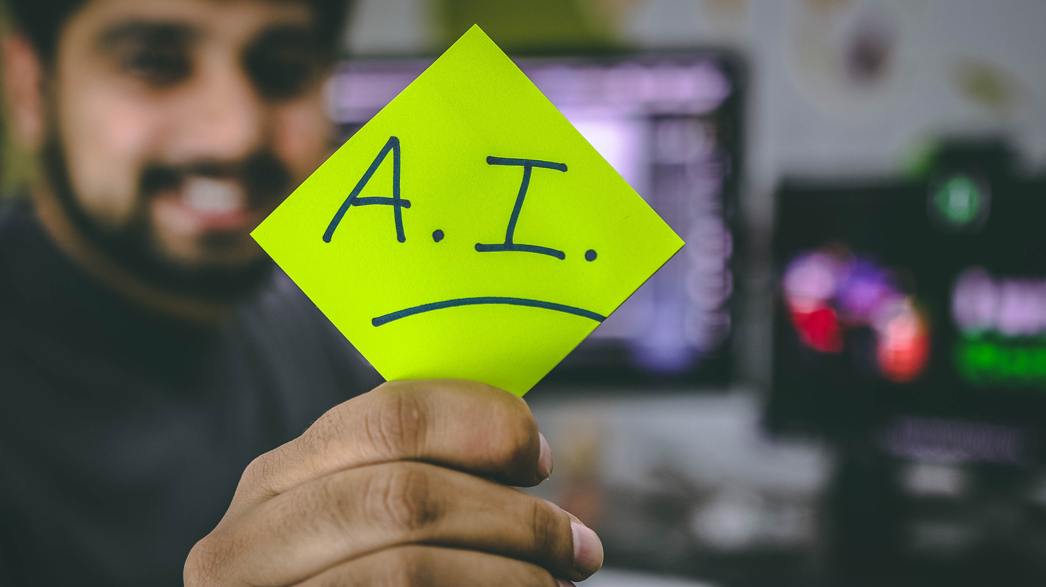 A man holding up a note reading "A.I.".