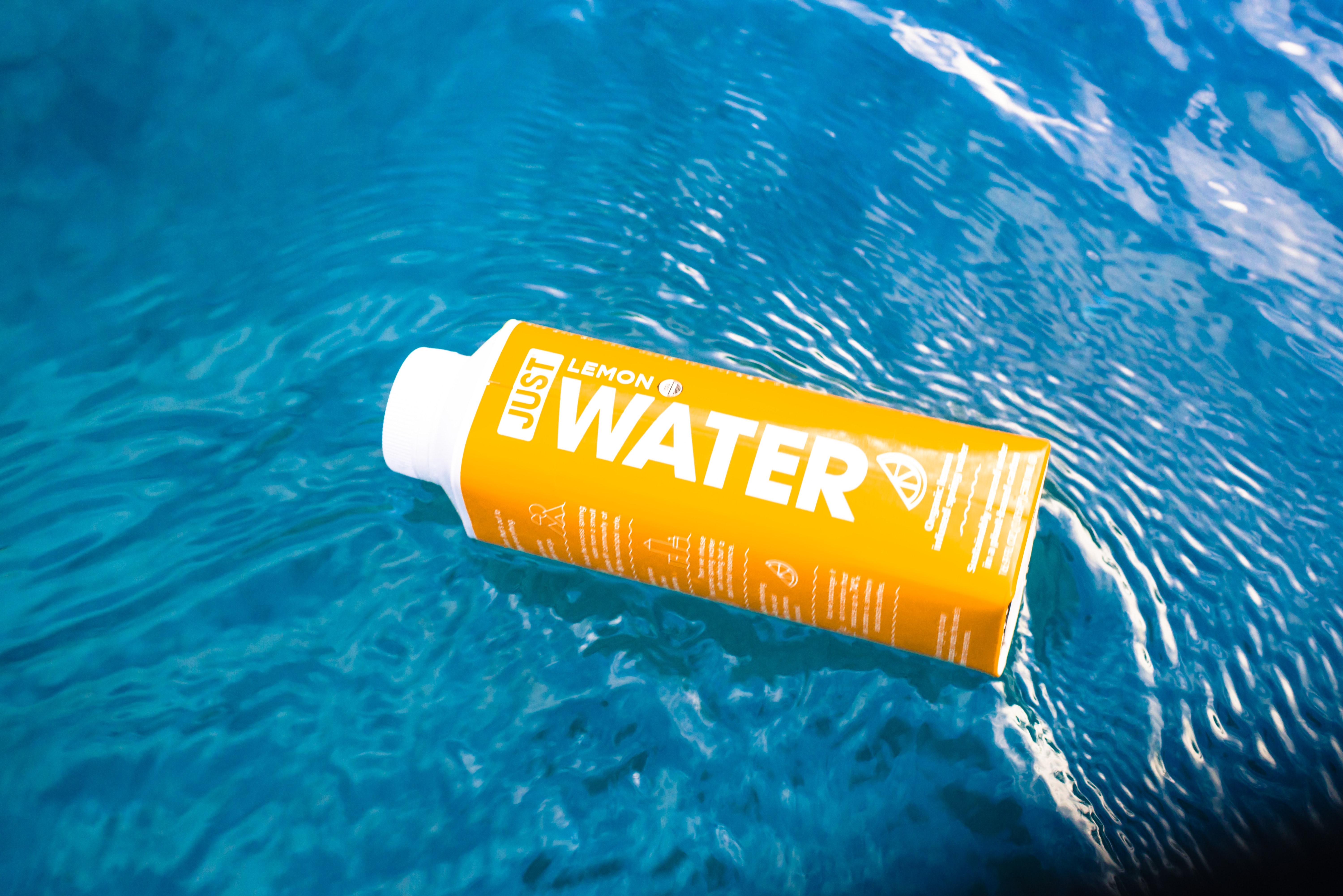 A carton of JUST water floating in a pool.