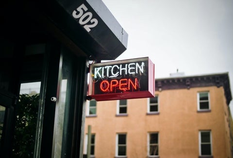 Outside a city center restaurant, a neon sign reads: "Kitchen open"