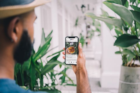 A man holds up a mobile phone with an Instagram post of a burger on it