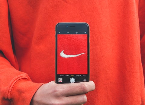 A man holds an iPhone up to his orange jumper, showing the Nike logo framed in the center