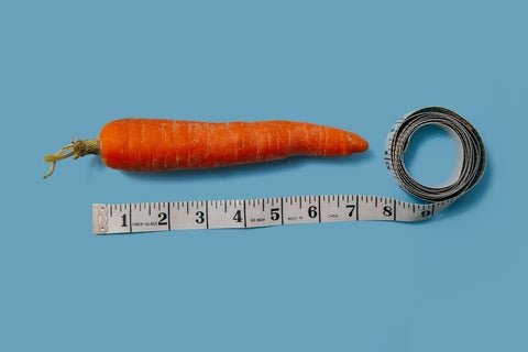 A carrot lies next to a tape measure on a light blue background