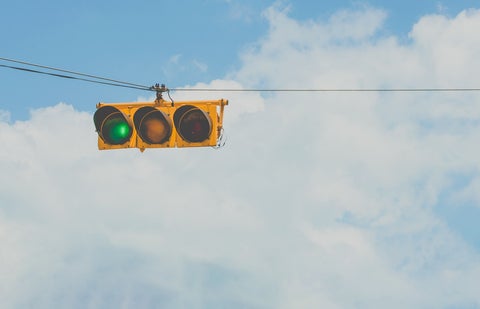 Traffic lights suspended from a wire against a blue, partially clouded sky. The green light is on.