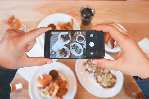 A person uses their phone to take a picture of plated meals on a table.