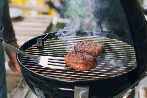 Outdoor barbecue with two Beyond Meat patties and a spatula that is about to flip one of them.
