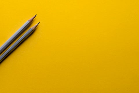 Two grey pencils against a bright yellow background