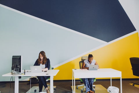 Two women sit, at work, at their desks