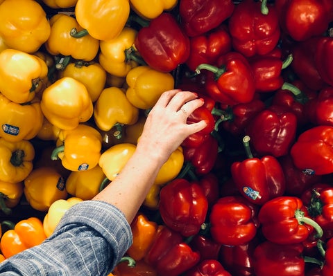 A woman's hand reaches for a red capsicum from a pile of red and yellow vegetables