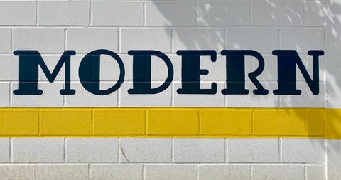 Hand-written wall sign in yellow, black and white that reads 'modern' in a serif typeface