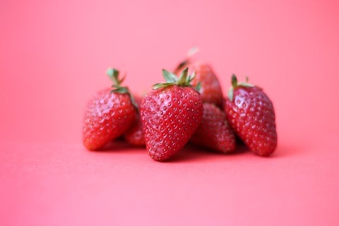 A small pile of strawberries set against a bubblegum pink background