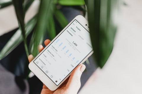 A woman holds a smartphone near a potted plant, displaying a social media analytics dashboard