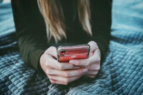 A woman holds a smartphone, while lying down