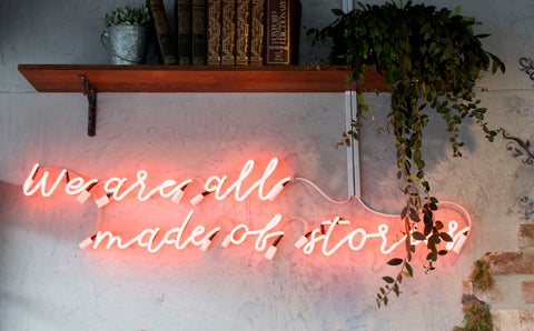 A neon wall sign that reads: "We are all made of stories"