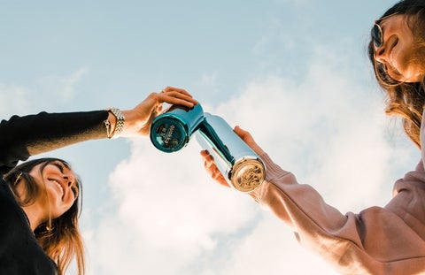 Two women cheers their KeepCups against a bright blue sky