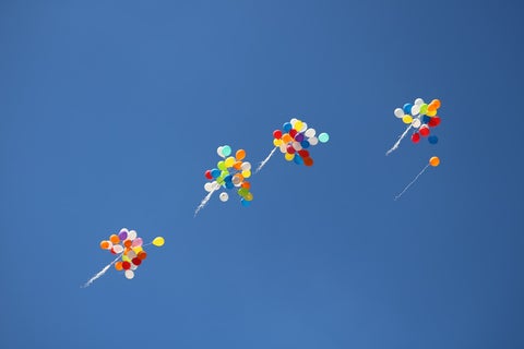 Four bundles of balloons rise up against a bright blue sky