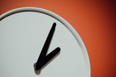 A white analogue clock set against a bright orange background