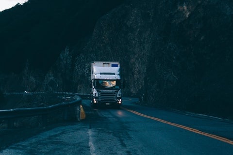 A large white truck drives down a dark, rural street