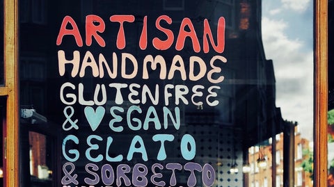 A hand-drawn sign on a window that reads "Artisan handmade gluten free & vegan gelato"