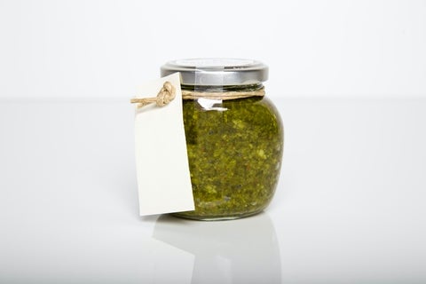 A plain glass of green pesto with a blank label