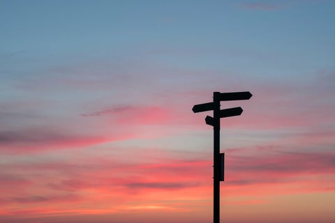 A street sign showing multiple directions set against a sunset