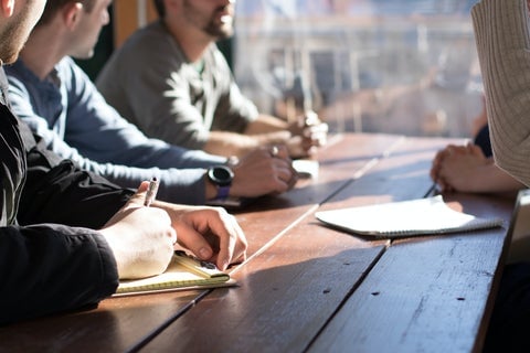 A group of men sat at a wooden table discussing some paperwork