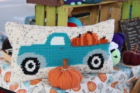A farmer's truck with pumpkins in the back, cross-stitched onto a cushion