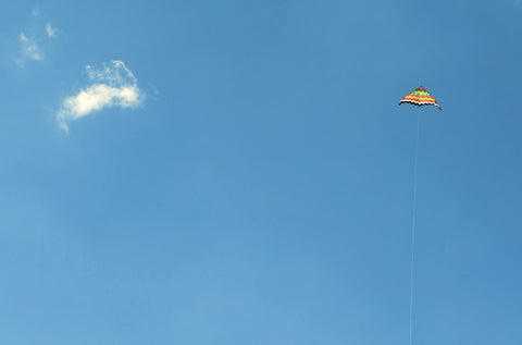 A colorful kite flies high in a bright, blue sky