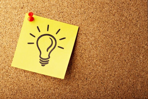 A yellow Post-It note with a lightbulb drawn on it, pinned to a brown corkboard
