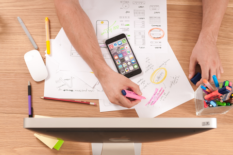 A bird's eye view of a man at a desktop computer, with pens and paper, drawing up a business plan