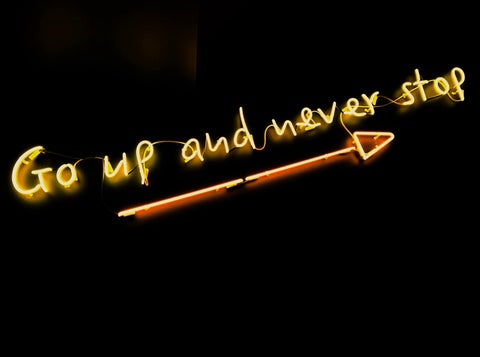 A yellow neon sign that reads 'Go up and never stop'