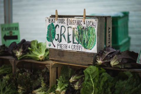 A farmers' market stall displaying lettuce and greens with a sign reading 'Eat your organic and local greens'