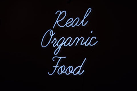 A light blue neon sign against a black background reading, in cursive, 'Real organic food'